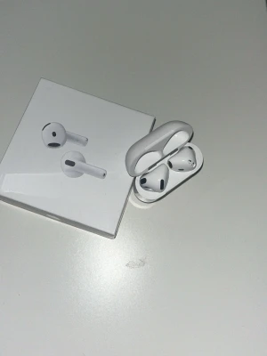 Apple AirPods med laddningsetui - Säljer ett par vita Apple AirPods med trådlöst laddningsetui. Snygg och stilren design i blank plast, klassisk AirPods-form med korta stjälkar och svarta detaljer. Kommer med originalförpackning. Den svarta ”delen” där uppe har gått av just därför säljer jag dem lite billigare. Dom funkar precis som dem ska, inget problem med dem. Dem är äkta. 