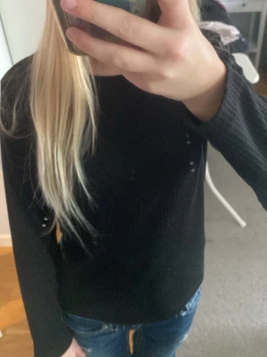 Svart ribbad topp med öppen rygg - Svart långärmad topp med ribbad struktur och snygg öppen rygg med korsade band. Perfekt till jeans för en cool och enkel look. Materialet känns mjukt och stretchigt.