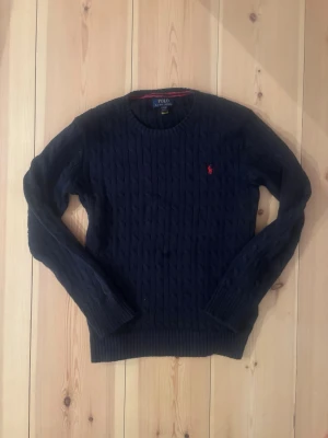 Mörkblå kabelstickad tröja Polo Ralph Lauren - Snygg mörkblå kabelstickad tröja från Polo Ralph Lauren 🔥 Klassisk modell med röd logga på bröstet – alltid rätt 🙌 Fint skick och riktigt skön att bära 😊 Pris är inte hugget i sten! 💸Äkta! Har du några frågor tveka inte att fråga 🤝 