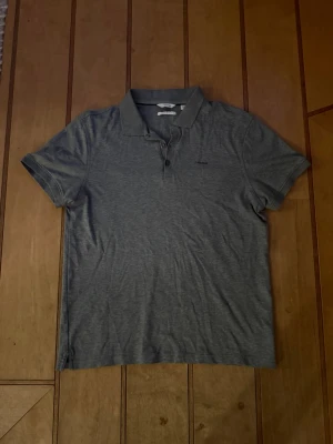 Grå piké från Calvin Klein - Snygg grå pikétröja från Calvin Klein med klassisk krage och knappar framtill. Tillverkad i mjuk bomull och har diskret logga broderad på bröstet. Perfekt till jeans eller shorts för en clean och enkel stil.