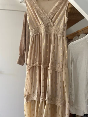 Beige långklänning med spetsdetaljer - Jag säljer en jättefin lång klänning med spets och guldiga detaljer, den passar perfekt för någon som är 170cm eller längre 💝 pris kan diskuteras