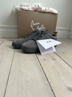 Gråa sneakers från Christian Louboutin - Snygga gråa sneakers från Christian Louboutin i mocka med matchande grå sula och snörning. Klassisk låg modell med stilren design och diskreta detaljer. Perfekta för dig som vill ha en exklusiv touch på din outfit. En lite defekt, se på sista bilden. Kvitto finns 