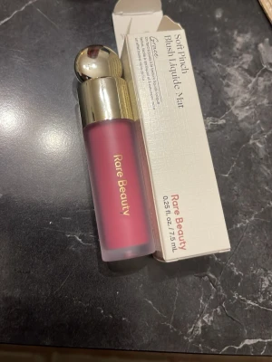 Rare Beauty Soft Pinch Liquid Blush - Flytande rouge från Rare Beauty i nyansen Soft Pinch. Kommer i en frostad glasflaska med guldfärgat lock och rund topp. Färgen är en djup rosa som ger ett fräscht och naturligt resultat. Förpackningen rymmer 7,5 ml och har en lyxig känsla.