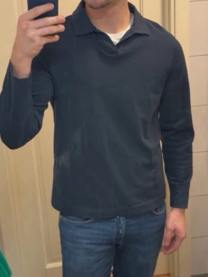 Mörkblå långärmad pikétröja - Snygg mörkblå långärmad pikétröja med klassisk krage och avslappnad passform. Tillverkad i mjukt bomullstyg som känns skönt mot huden. Perfekt för dig som gillar en clean och stilren look.