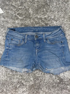 Blå jeansshorts från Pepe Jeans - Säljer ett par klassiska blå jeansshorts från Pepe Jeans med rå kant nertill och femficksmodell. Shortsen har låg midja, knappgylf och slitna detaljer för en avslappnad look. Perfekta till sommaren! Jag har klippt de själv 🤗