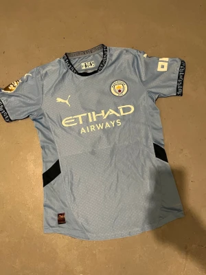 Manchester City matchtröja Haaland #9 - Ljusblå Manchester City matchtröja från Puma med Haaland och nummer 9 på ryggen. Tröjan har klubbmärke, Etihad Airways-tryck och svarta detaljer på sidorna. Korta ärmar och sportig passform, perfekt för fotboll eller träning.