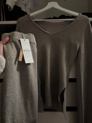 Glittrigt set från Bitici - Snyggt tvådelat set från Bitici i glittrande silverfärgat material. Setet består av en långärmad topp med v-ringning och matchande byxor med resår i midjan. Materialet har en skimrande effekt som ger en lyxig känsla. Perfekt för dig som vill sticka ut.