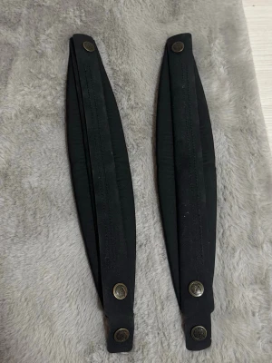 Svarta fjällräven breda tygbälten med knappar för ryggsäck  - Två svarta bälten i tyg med bred form och dekorativa metallknappar i mässingfärg. Bältena har en stilren och enkel design, perfekta för att ge outfiten en cool touch. Fjällräven, för ryggsäckar kånken som skydd mot kroppen helt nytt 