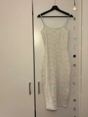 Pastellfärgad mönstrad klänning - Säljer en snygg långklänning med smala axelband och vågigt pastellmönster i mintgrönt, rosa och vitt. Klänningen har en kroppsnära passform och är perfekt för sommarens alla tillfällen. Materialet känns mjukt och stretchigt.