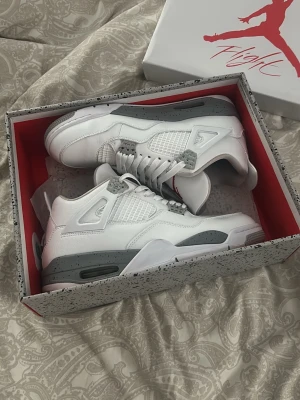 Air Jordan 4 White Oreo sneakers - Snygga Air Jordan 4 White Oreo sneakers i vitt läder med grå och svarta detaljer samt röda inslag på plösen. Klassisk siluett med meshpaneler på sidorna och stabil sula. Perfekta för dig som vill sticka ut med stilrena och ikoniska sneakers.