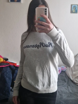 Ljusgrå sweatshirt från Peak Performance - Ljusgrå sweatshirt från Peak Performance med mörkblå logotyp på bröstet. Tröjan har rund halsringning, långa ärmar och ribbade muddar vid ärmslut och nederkant. Perfekt för en avslappnad och sportig stil. Känns mer som en S/xs. 