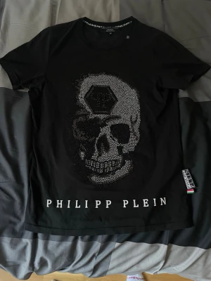 Svart Philipp Plein t-shirt  - Svart t-shirt från Philipp Plein, endast fått komplimanger från den. Har använt den BÄLDIGT sparsamt, eftersom den har alltid varit min favorit T-shirt, men bäst lite ur den. Priset är ej hugget i sten, hör av dig vid minsta lilla fundering!