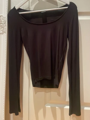 Svart tight långärmad topp från Gina Tricot i storlek S  - En svart långärmad topp med slits i ärmarna från Gina Tricot med bred, rundad urringning. Tunn och stretchig i materialet, perfekt för lager på lager eller som enkel statement-piece. Snygg och enkel att styla till olika looks.