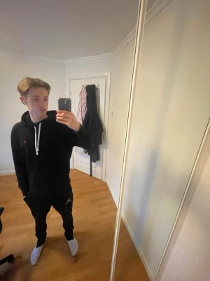 Svart hoodie från Polo Ralph Lauren - Säljer en svart hoodie från Polo Ralph Lauren med vit dragsko och klassisk röd logga på bröstet. Hoodien har stor huva och magficka framtill. Perfekt för en chill och stilren look.