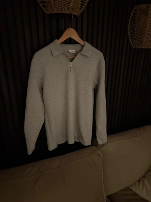 Grå långärmad tröja med halv dragkedja - Snygg grå långärmad tröja med krage och halv dragkedja framtill. Tröjan har en enkel och stilren design som passar till det mesta. Tillverkad i mjukt material för extra komfort.