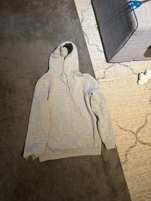 Ljusgrå basic hoodie med huva - En stilren ljusgrå hoodie med huva och dragsnören. Hoodien har långa ärmar, ribbade muddar vid ärmslut och nederkant samt en klassisk passform. Perfekt för en avslappnad och enkel look. Materialet känns mjukt och bekvämt, troligen bomullsblandning.