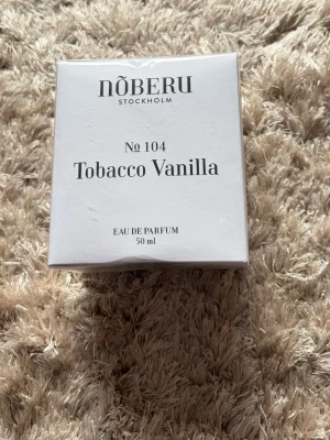 Nõberu Tobacco Vanilla EdP 50 ml - Nõberu Tobacco Vanilla No 104 Eau de Parfum är en parfym i elegant vit kartong. Doften kombinerar varma toner av tobak och vanilj. Flaskan rymmer 50 ml och förpackningen har stilren, minimalistisk design med svart text.