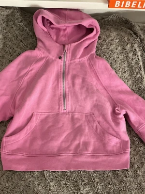 Rosa hoodie från Lululemon med dragkedja - Snygg rosa hoodie från Lululemon med halv dragkedja framtill och stor känguruficka. Tillverkad i mjuk bomullsblandning och har en rejäl huva. Perfekt för chill dagar eller när du vill ha en sportig look. Passar ifrån xs till m 
