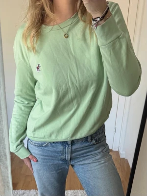 Ljusgrön sweatshirt från Paul Smith - Ljusgrön tröja från Paul Smith med rund halsringning och långa ärmar. Tröjan har en liten broderad zebra-logga på bröstet och ribbade muddar vid ärmslut och nederkant. 100% bomull och supersöt till sommaren!