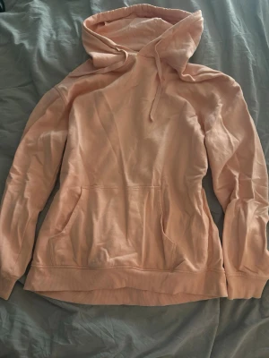 aprikosfärgad hoodie från C - Mysig aprikosfärgad hoodie från C med klassisk huva och känguruficka framtill. Fin till sommaren. Tillverkad i mjukt bomullsmaterial och har ribbade muddar vid ärmslut och nederkant. Perfekt för en chill och avslappnad stil.