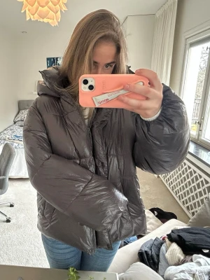 Mörkgrå pufferjacka med huva - Säljer en riktigt fet mörkgrå pufferjacka med stor huva och breda kanaler. Jackan har en glansig finish och stängs med dragkedja och knappar. Perfekt för kalla vinterdagar och ger en cool oversized look. Passar ca ❤️Ny utan prislapp!!