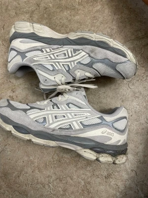 Gråvita Asics sneakers - Snygga sneakers från Asics i grått och vitt med klassisk mesh och mockadetaljer. Skorna har en sportig siluett, tydlig logga på sidan och robust sula för extra komfort. Perfekta för dig som gillar retrovibbar och streetstyle.