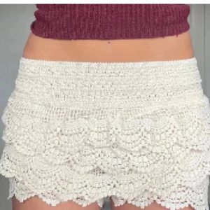 Vita virkade shorts med volang - Snygga vita virkade shorts med flera lager volangdetaljer. De har hög midja och ett elastiskt midjeband för skön passform. Perfekta för sommarens alla äventyr och ger en bohemisk vibe till din outfit.