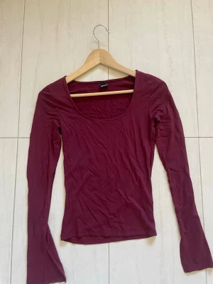 Vinröd långärmad topp Gina Tricot - Säljer en vinröd långärmad topp från Gina Tricot. Toppen har en djup rundringning och är i ett mjukt, stretchigt material som sitter tight mot kroppen. Perfekt att styla med jeans eller kjol för en enkel men snygg look.