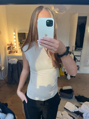 Beige ärmlös topp i stretchigt material - Säljer en enkel och stilren beige topp som är ärmlös och har en tight passform. Materialet känns stretchigt och mjukt, perfekt till jeans eller kjol. Toppen har en rund halsringning och är helt utan mönster eller detaljer.