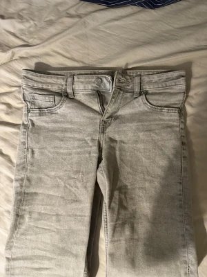 Ljusgrå utsvängda jeans  - Säljer ett par ljusgrå jeans med flared passform och klassisk femficksdesign. Jeansen har bälteshällor och stängs med knapp och dragkedja. Perfekta för en avslappnad och stilren look. Materialet är denim.