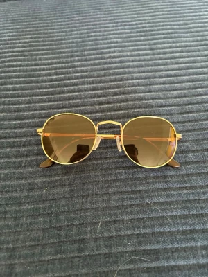 Runda solglasögon med guldfärgade bågar - Snygga runda solglasögon med tunna guldfärgade metallbågar och bruna glas. Klassisk retrostil som passar perfekt till sommaren. Lätta och bekväma att bära med justerbara näskuddar.