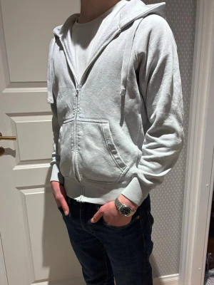 Ljusgrå zip hoodie med huva ifrån Russemerch - Säljer en ljusgrå hoodie med dragkedja och huva. Hoodien är i märket Russemerch/Russedress. Hoodien har fickor framtill, ribbade muddar och snören i huvan. Perfekt för chill dagar eller när du vill ha en enkel och clean look. Materialet är mjukt och skönt, troligtvis bomullsblandning. Gott skick, dvs. 8/10.