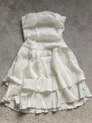 Vit axelbandslös kortklänning - Säljer denna supersöta klänningen! Använd 1-2 ggr. Hör av er vid frågor och funderingar ❤️