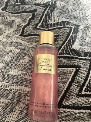 Victoria's Secret rosa Temptation Shimmer bodymist/parfym - En lyxig shimmer body mist från Victoria's Secret i doften Temptation. Flaskan är rosa med guldigt lock och etikett. Bodymisten är i 250 ml knappt använd  och är i dofterna Lucious Apple,desert flower och shimmer obsessed. Parfymen passar dig bra om du gillar söta eller fruktiga dofter. 