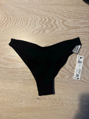 Svarta bikiniunderdelar från Lindex - Snygga svarta bikiniunderdelar i modellen Brazilian från Lindex. Klassisk och enkel design med smalare passform bak. Tillverkade i mjukt och stretchigt material som passar perfekt till stranden eller poolen. Aldrig använd med prislapp kvar
