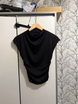 Svart topp  - Säljer en svart top med korta ärmar. Modellen är lite lösare upptill och smalnar av nedtill, vilket ger en snygg siluett. Perfekt att matcha med jeans eller kjol för en trendig look. Jag är inte säker på vart den är ifrån tror hm