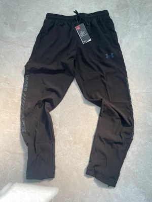 Svarta träningsbyxor från Under Armour - Svarta träningsbyxor från Under Armour med elastisk midja och dragsko. Byxorna har logga på vänster lår och text längs benet. Perfekta för gymmet eller löprundan, tillverkade i lätt och funktionellt material. Storlek: S. Nya med prislapp! Pris går att diskutera🙌🏻