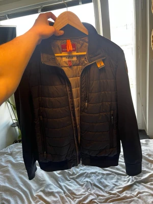 Svart jacka från Parajumpers - Säljer en svart jacka från Parajumpers med quiltad front och rygg, samt släta ärmar. Jackan har två dragkedjeförsedda fickor fram och en klassisk gul Parajumpers-detalj vid kragen. Perfekt för kalla dagar.