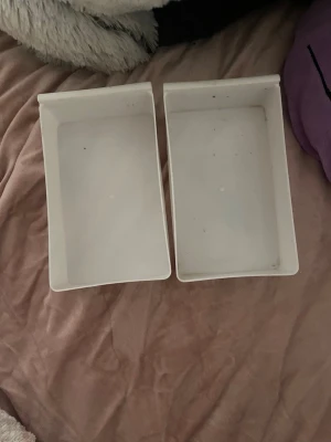 Vita plastlådor för förvaring - Två rektangulära vita plastlådor perfekta för förvaring av småsaker, smink eller kontorsmaterial. Lådorna har enkel design och släta kanter, vilket gör dem lätta att stapla eller placera i hyllor och lådor. Praktiska att använda i hemmet eller på kontoret.