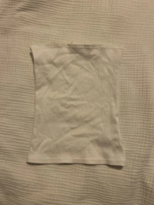 Vit ribbad bandeau tubtopp - Säljer en enkel och stilren vit bandeau tubtopp i ribbad bomull. Perfekt att matcha med jeans eller kjol för en clean look. Toppen är ärmlös och har en tight passform som sitter snyggt på kroppen.