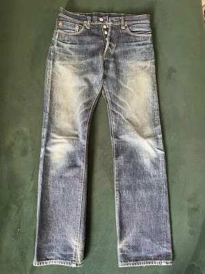 SKIT FETA MOMONTARO  - Säljer ett par blå jeans med raka ben och snygga slitningar framtill och baktill. Jeansen har klassisk femficksdesign, knäppning med knappar och kontrastsömmar. Materialet är denim i bomull och de har en vintage tvättad look.