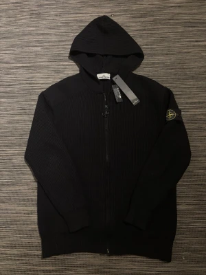 Svart zip hoodie från Stone Island - Säljer en riktigt snygg svart hoodie från stone lsland! Hoodien är i mycket bra skick och har inga defekter. Perfekt nu till sommarkvällarna☀️Tröjan är 100% äkta. Ribbstickad och full zip. Om ni har några frågor så är de bara att höra av er!