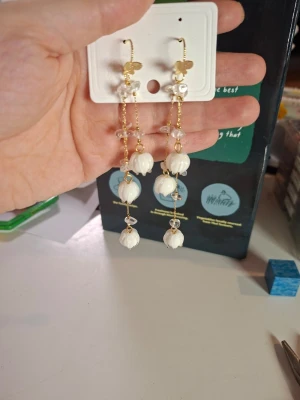 Långa örhängen med vita pärlor - Säljer ett par långa örhängen med vita pärlor och guldfärgade detaljer. Örhängena har små blommor och fjärilar upptill samt genomskinliga pärlor längs kedjan. Perfekta för dig som gillar unika accessoarer med romantisk vibe.