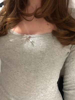 Ljusgrå ribbad topp med rosett - Supersöt ljusgrå ribbad topp med lång ärm och liten rosett framtill. 🎀🎀