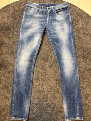 Mörkblå slitna dondup jeans  - Säljer ett par blå jeans från Dondup med slitningar och tvättade detaljer. Jeansen har klassisk femficksmodell, låg midja och smal passform. Materialet är denim i bomull och de har en cool, använd look med små hål och slitna partier.
