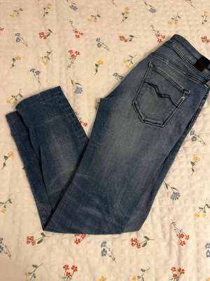 Blå slim fit jeans från Replay - Säljer ett par blå slim fit jeans från Replay med klassisk femficksdesign och snygga slitningar. Jeansen har en diskret logga på bakfickan och är tillverkade i mjukt denimtyg som ger en skön passform. Perfekta till en avslappnad stil.Ett par fina replay jeans   Den är uppsyd lite vid foten men inte så mycke kanske bara några centimeter och har några nackdelar som du kan se på bilderna annars jätte fina replay jenas. I midjan är den stressig så den ska sitta bra.mått👇   Midjan 35 cm   Längden 90c