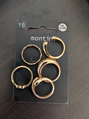 Guldfärgade ringar från Montini - Snyggt set med fem guldfärgade ringar från Montini. Ringarna har olika former, en med tvinnad design och en dekorerad med små pärlor. Perfekt för att mixa och matcha till din stil. Metallmaterial och trendig look.