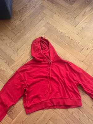 Röd cropped hoodie från H&M Divided - Snygg röd cropped hoodie från H&M Divided med huva och dragsko. Tillverkad i mjukt bomullsmaterial och har en avslappnad passform. Perfekt för en chill och trendig look.