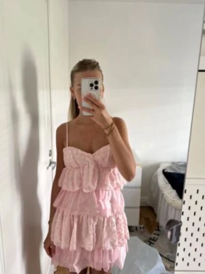 Rosa volangklänning med spetsdetaljer - Söt rosa kortklänning med tunna axelband och flera lager volanger. Klänningen har spetsdetaljer och en stor rosett framtill som ger en romantisk känsla. Perfekt för sommarens alla tillfällen. Helt slutsåld!