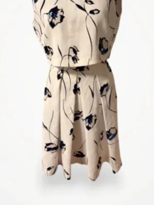 Blommig vit klänning med blå detaljer - Snygg vit klänning med blå och svarta blommor, v-ringad och ärmlös. Kjolen är kort och har ett lätt utställd passform. Perfekt för sommarens varma dagar och har en fräsch, ungdomlig stil.